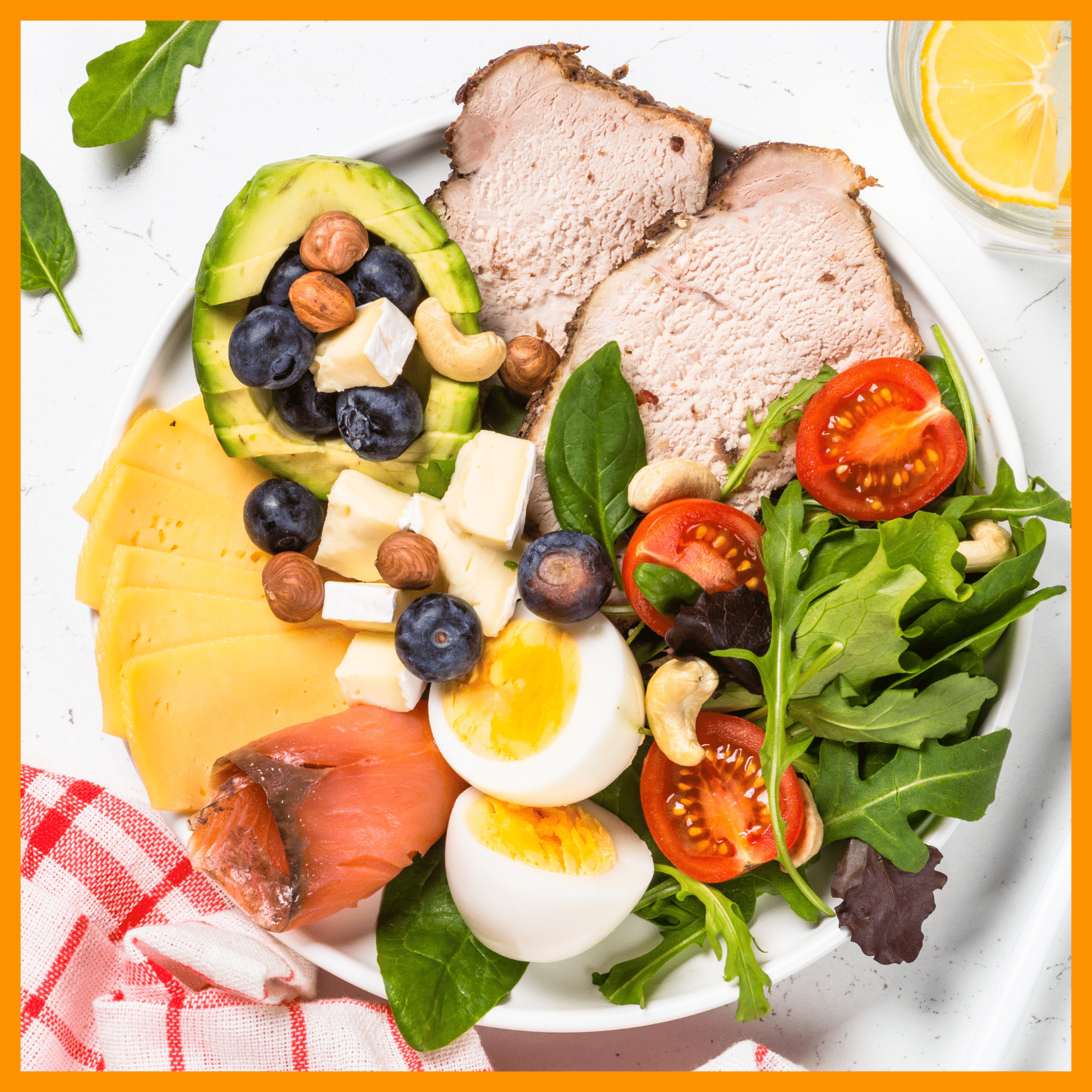 Home 2 Keto bowl with roast pork, avocado, eggs, cheese, smoked salmon, nuts, fresh greens, and tomatoes on a white plate.