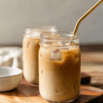 Mason jars of iced protein coffee with golden straws on a wooden board