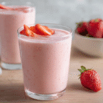 Glass of strawberry protein smoothie topped with sliced strawberries on a wooden surface