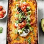 Keto taco lasagna topped with avocado, sour cream, olives, and tomatoes in a loaf pan