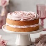 Two-layer keto vanilla cake with pink frosting on a white cake stand