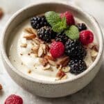 Keto yogurt in a ceramic bowl topped with berries and chopped nuts