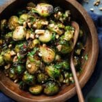 Kung Pao Brussels sprouts in a wooden bowl topped with peanuts and herbs