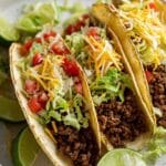 Close-up of keto beef tacos with ground beef, shredded lettuce, cheese, tomato, and lime wedges