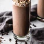 Chocolate protein shake in tall glass with chocolate chip topping