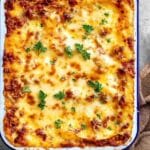 Baked protein pasta casserole topped with golden melted cheese and fresh parsley in a white enamel baking dish.