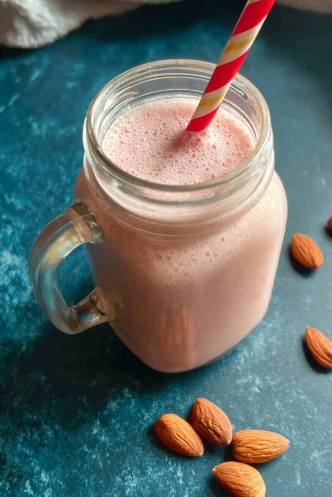 Low Calorie Protein Shake That’s Delicious, Quick & Body-Goal Friendly 1 Pink protein shake in mason jar with striped straw and almonds.