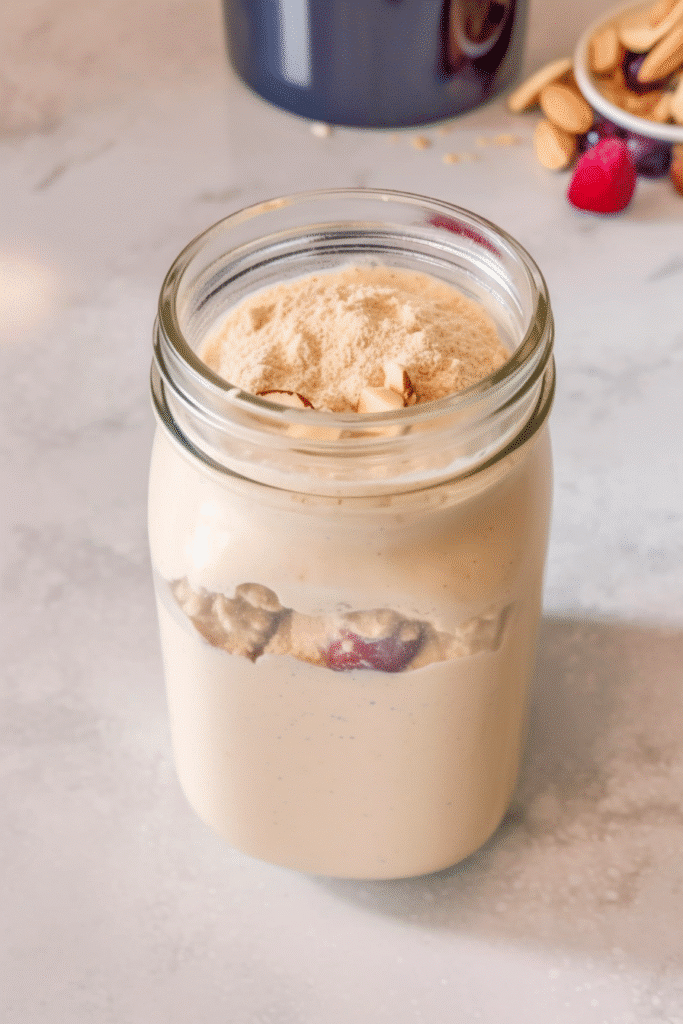 Low Calorie Protein Shake That’s Delicious, Quick & Body-Goal Friendly 4 Low calorie protein shake in a glass jar, topped with almond slices and protein powder, set on a light marble surface.