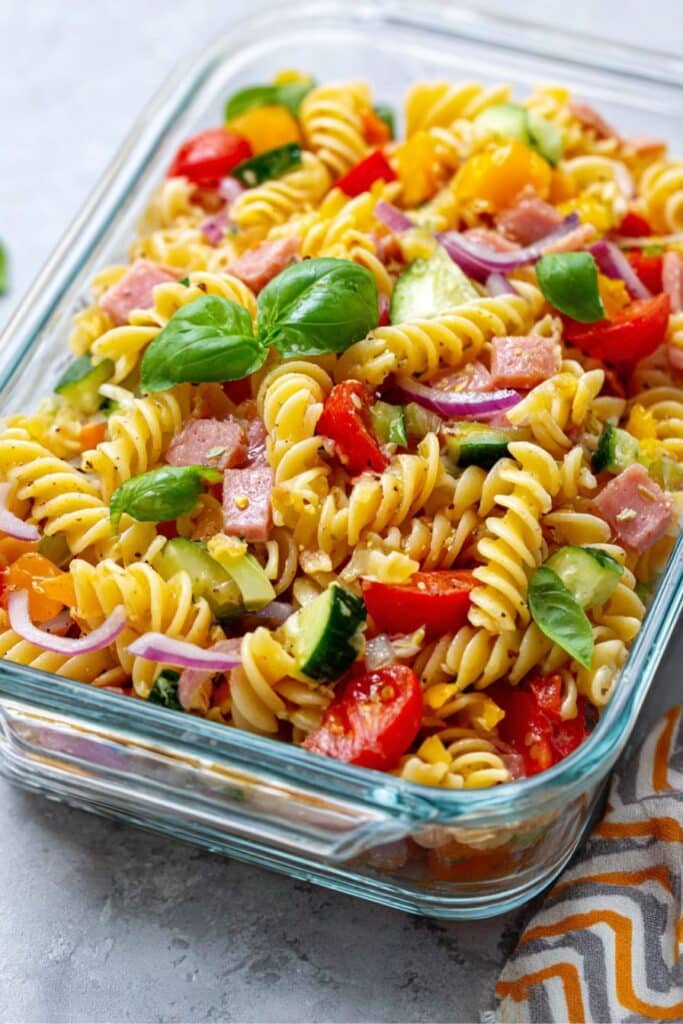 High Protein Italian Pasta Salad That’s Bold, Fresh, and Filling 1 Close-up of a colorful high protein pasta salad with rotini, ham, cherry tomatoes, cucumber, red onion, and basil in a glass dish.